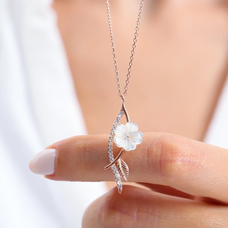 damski srebrny naszyjnik wisiorek Flower 2 kwiat to esencja subtelnej elegancji. Jego zawieszka przedstawia białą kwiatową formę obok której delikatnie mieni się liść i łagodnie wygięta łodyga wysadzana drobnymi kamieniami senka srebro 925